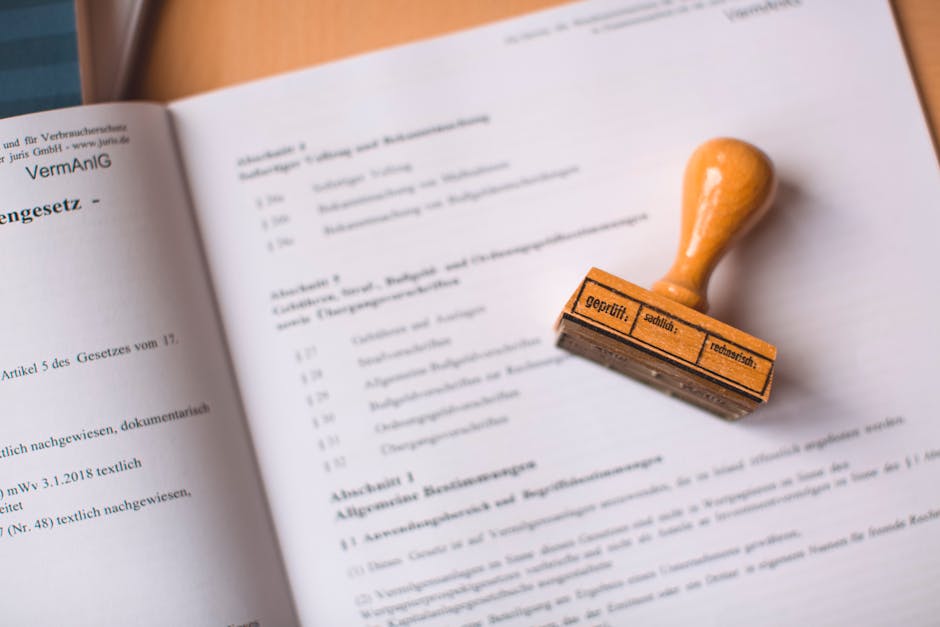 A close-up view of an open document featuring printed legal or official text in a foreign language, resting on a flat surface. To the right of the document, a rubber stamp with an orange handle and a